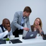 A diverse team collaborating in a modern office environment, discussing work on a laptop.